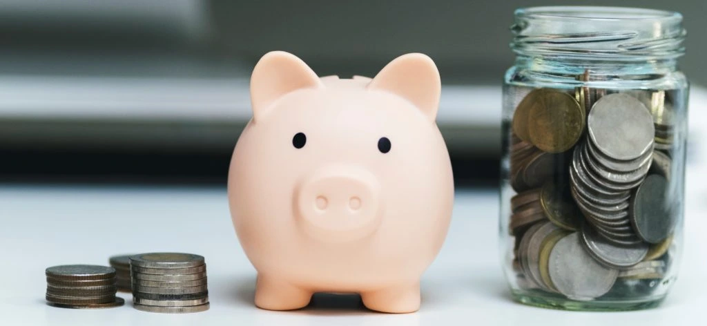 A piggy bank beside a jar of saved coins